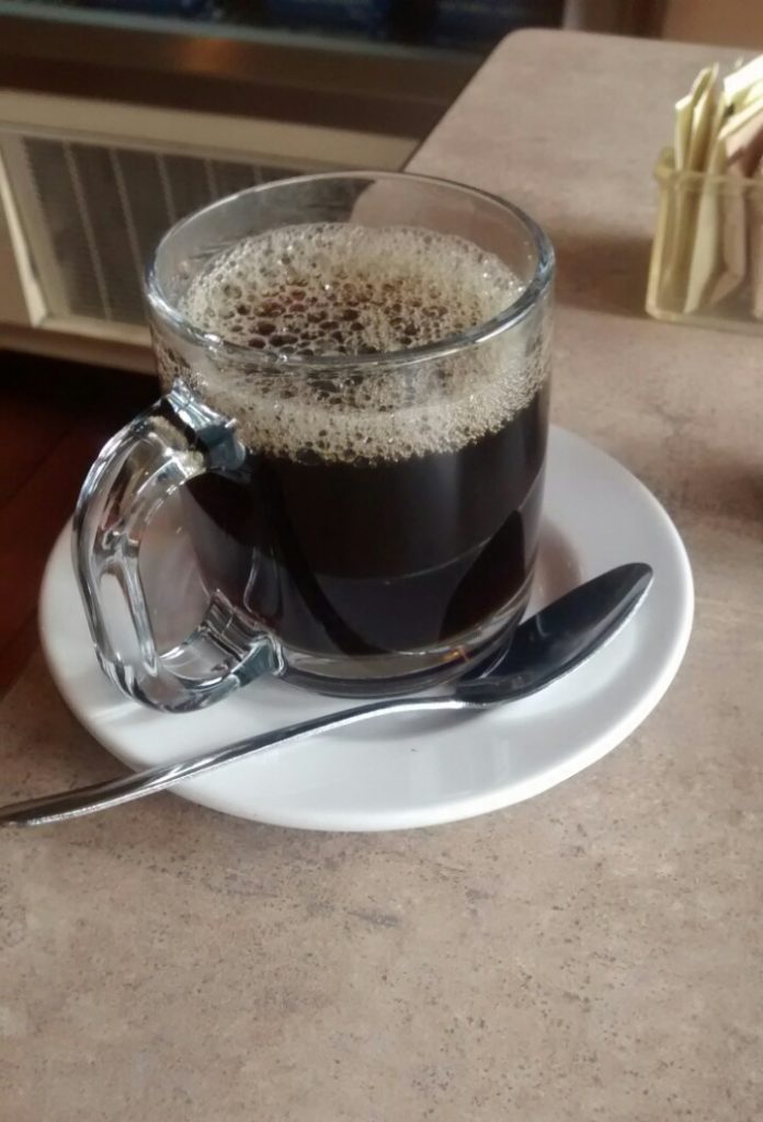 Mug of black coffee on a saucer with a spoon